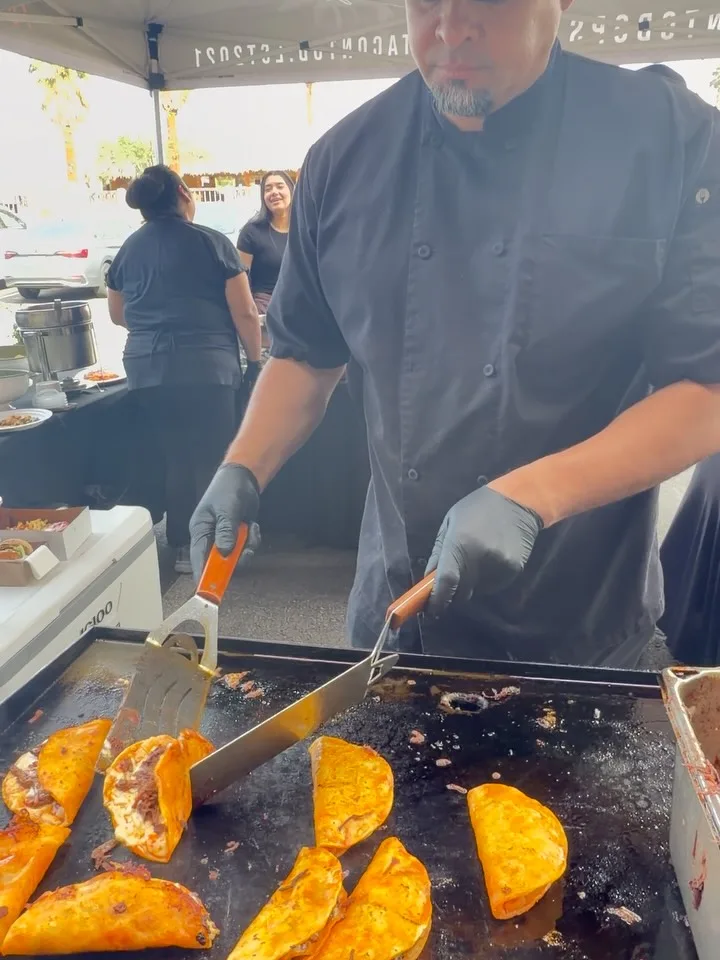 Omar, TacoNTodo owner, grilling birria tacos on the flattop at a catering event